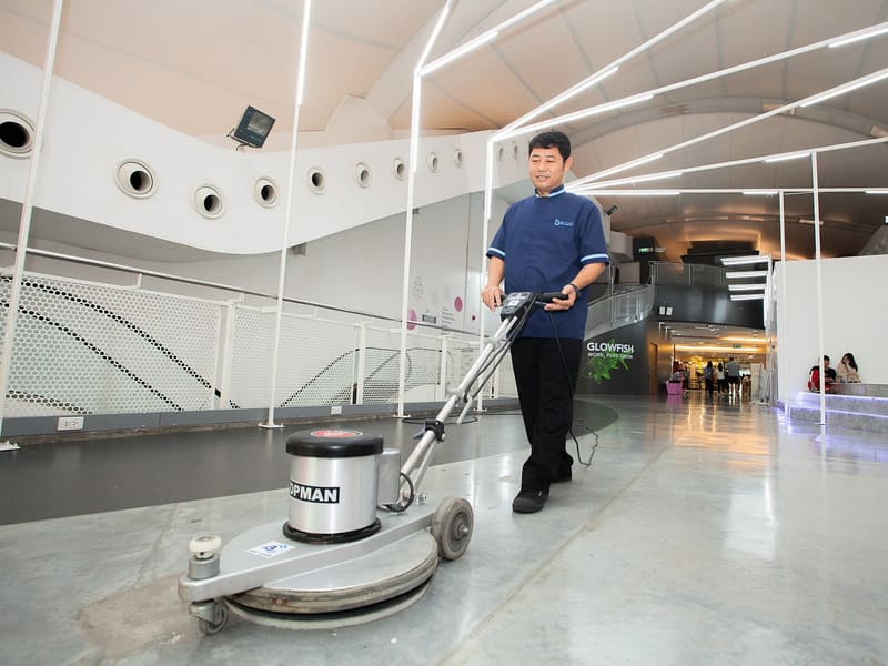 Agent d’entretien guidant une monobrosse sur un sol en béton lissé dans un bâtiment commercial